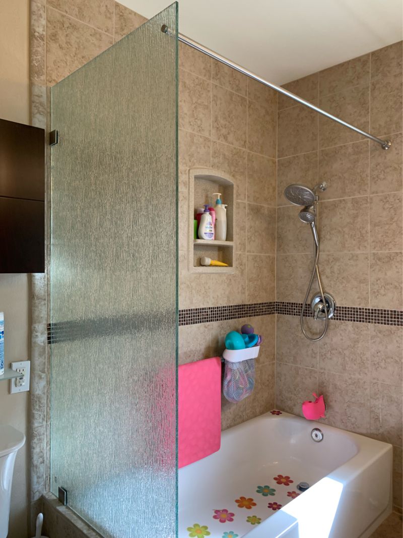 Patterned rain-glass splash panel with a through-glass curtain rod over a tub