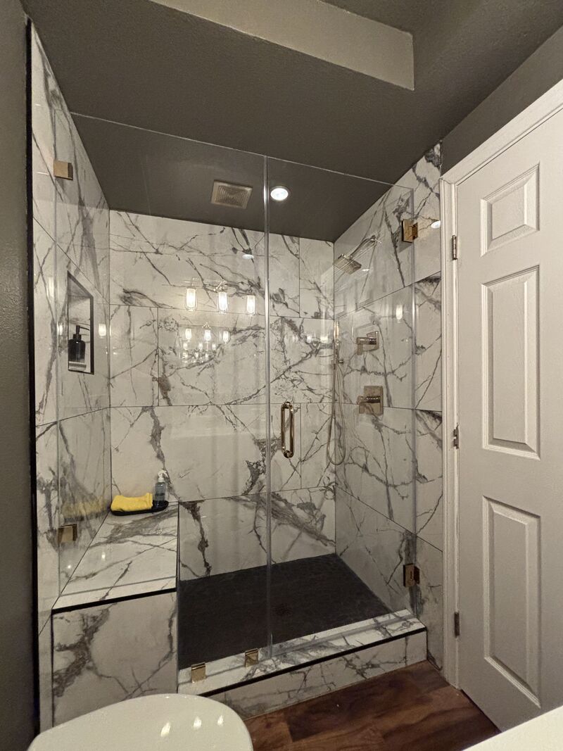 Frameless shower door and inline panel at a bench with polished brass hardware in Huntington Beach