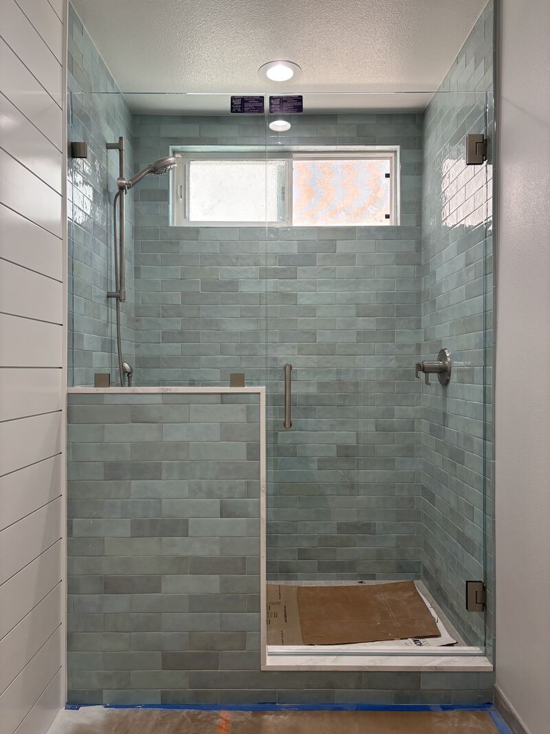 Frameless shower door with an inline panel adjoining a pony wall in Huntington Beach