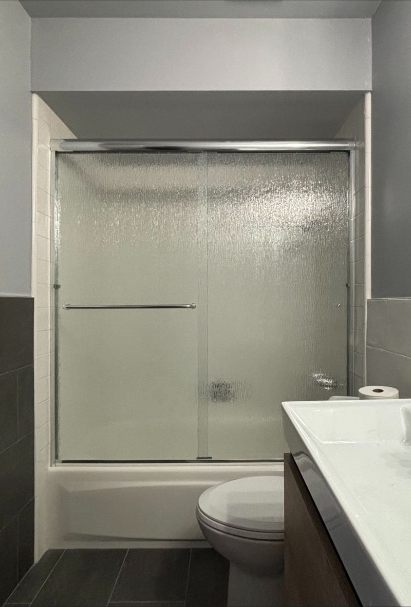Rain-glass bypass sliding shower enclosure installed on a steel tub in Huntington Beach