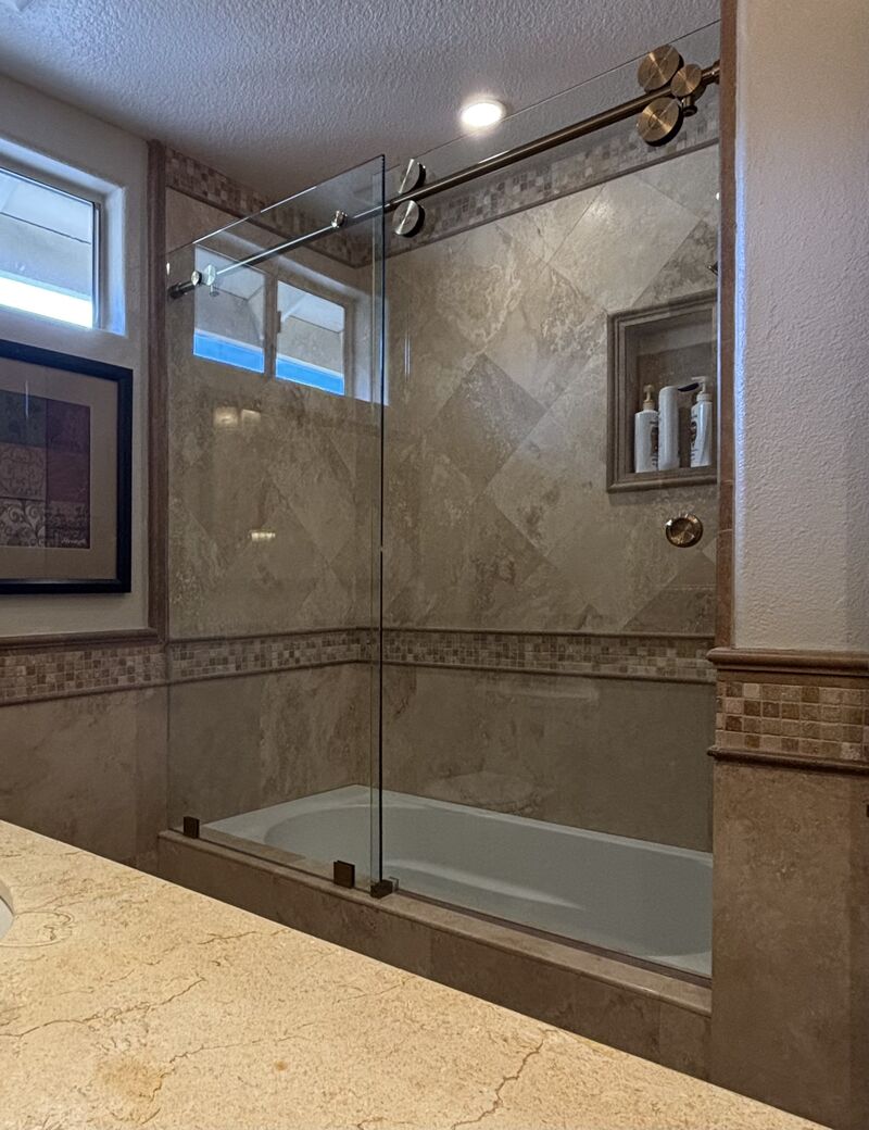 Euroglide sliding shower enclosure with gold hardware on a travertine tub deck in Laguna Niguel