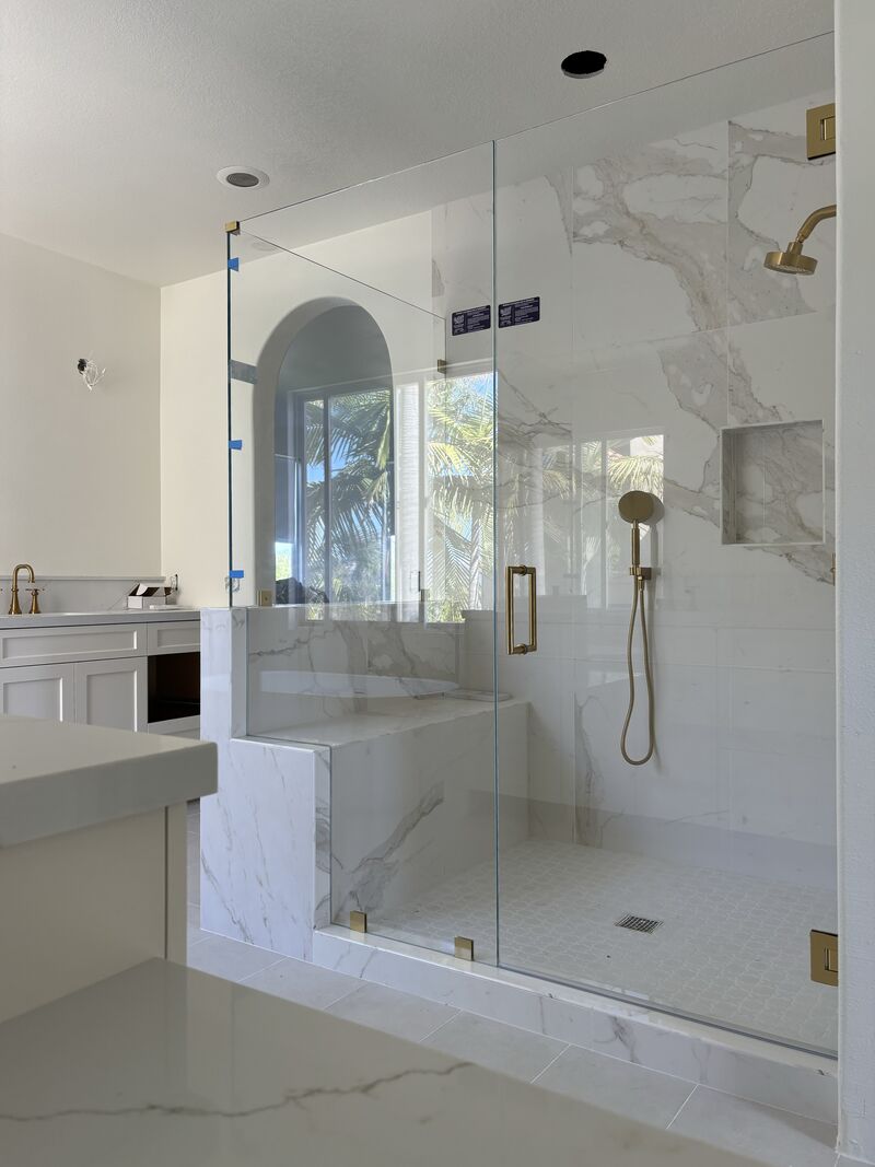 Low-iron frameless shower enclosure notched for a bench and pony wall with satin-brass hardware in Laguna Niguel