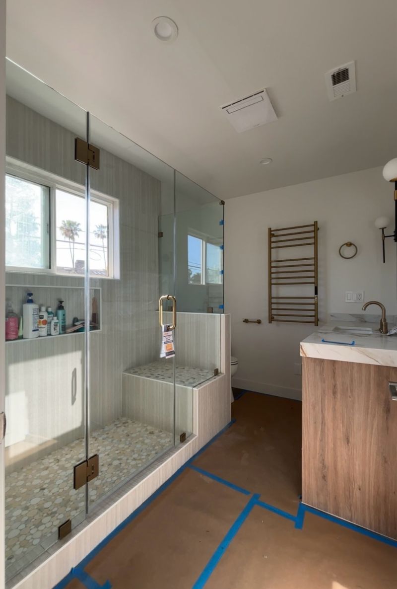 Frameless corner shower enclosure notched around a bench and pony wall in Long Beach
