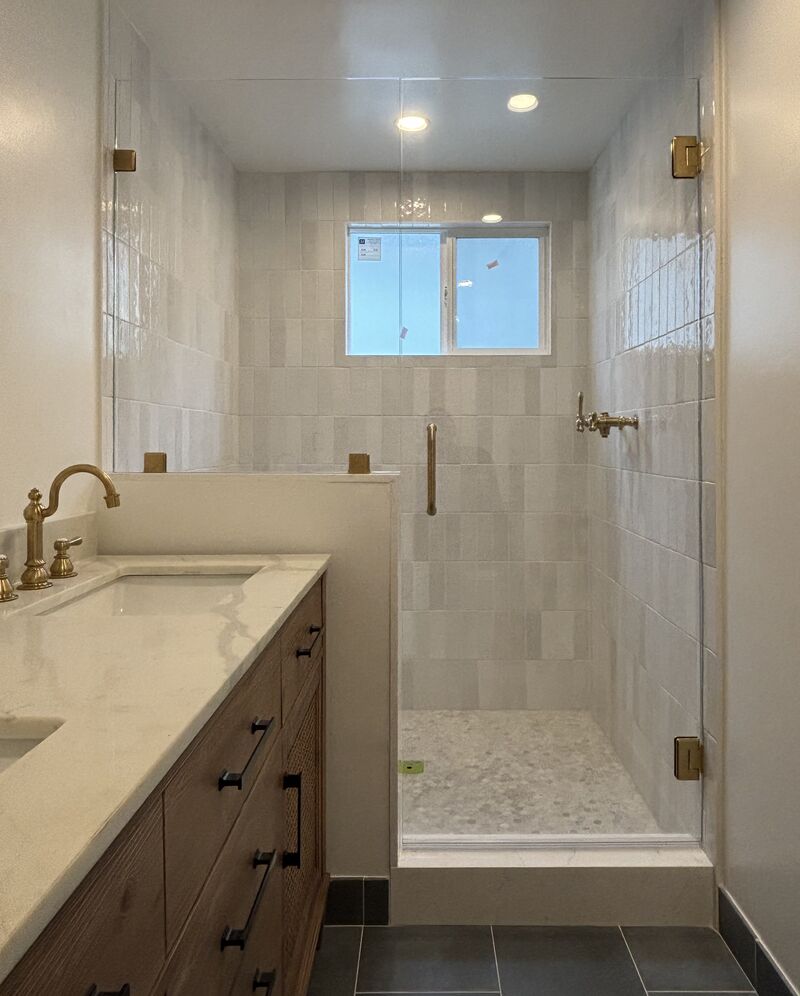 Frameless shower door and inline panel on pony wall with brushed-gold hardware in Manhattan Beach