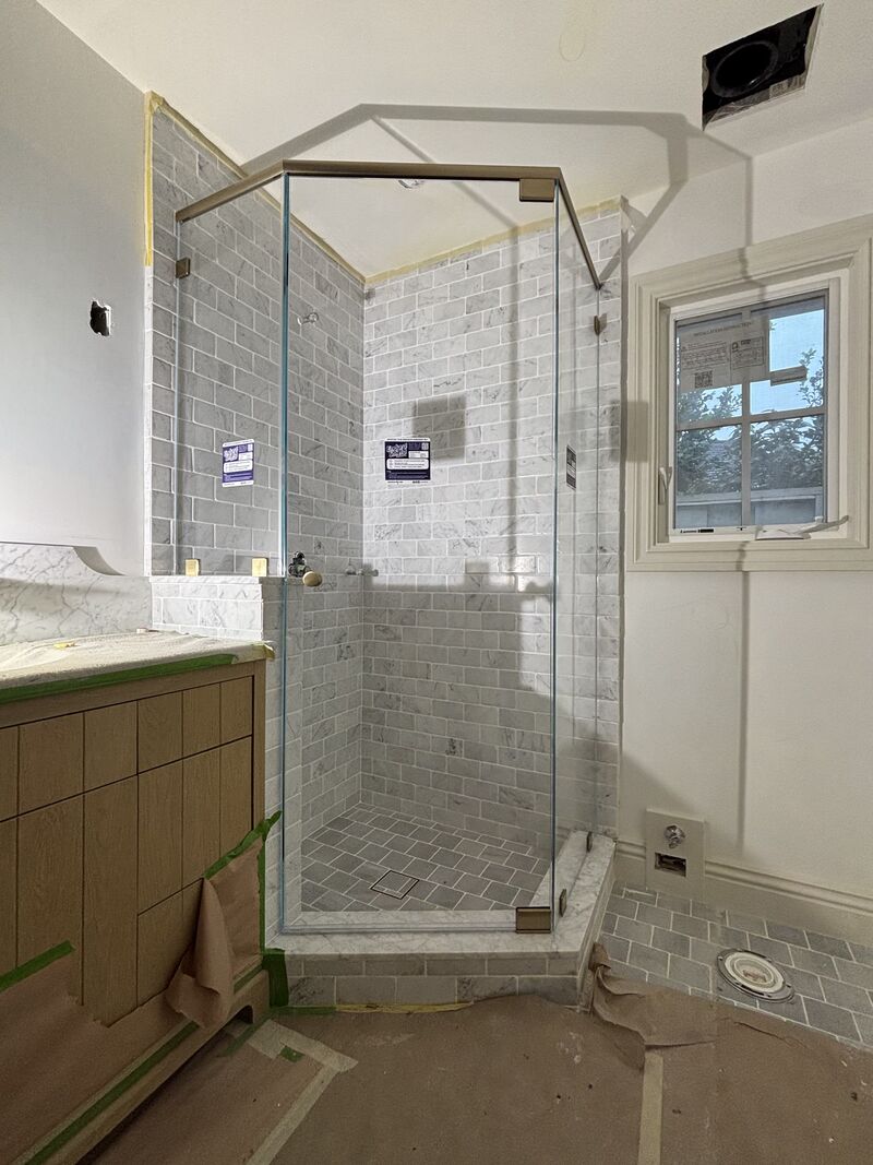 Opti-White low-iron neo-angle shower enclosure with brushed-bronze header on a pony wall in Newport Beach