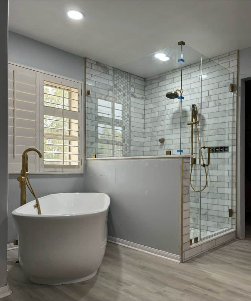 Brushed-gold corner shower on a wide pony wall beside a freestanding tub in Oceanside
